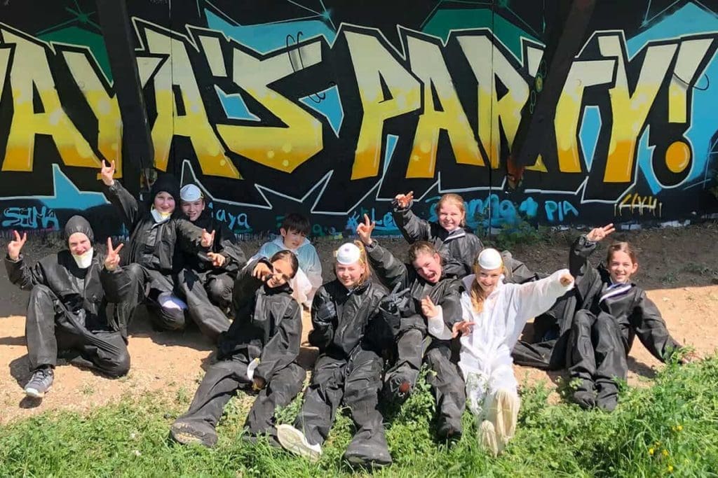 Um den Graffiti Kindergeburtstag von Maya gebührend zu feiern, haben wir von Graffiti Stuttgart mit ihren Gästen ein cooles Graffiti an der Außenwand vom Camp Feuerbach gemalt. Am Tag der Malaktion grundierte Micha die zu besprühende Fläche mit Wandfarbe, um dann die zuvor verabredeten Motive auf der Betonmauer vor zu skizzieren. Anschließend malte Maya mit ihren Freunden den Graffiti Style mit allen Buchstaben und Elementen farbig aus. Danach sprühte Micha noch die Konturen Outlines und die Lichteffekte.