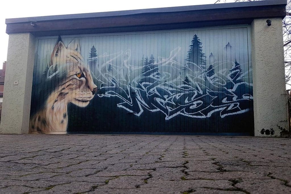 Für die Familie Riethmüller aus Leonberg haben wir das triste Garagentor mit einem tollen Wildnis Motiv gestaltet. Chris sprühte über mehrere Ebenen einen Wald im Nebel, einen Luchs und einen Wildnis Schriftzug.