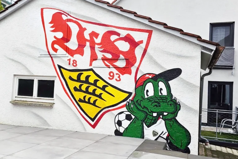 Eine weiß gestrichene Garagenwand mit einem Graffiti des VfB Stuttgart-Wappens und dem grün lächelnden Maskottchen Fritzle, der einen Fußball hält