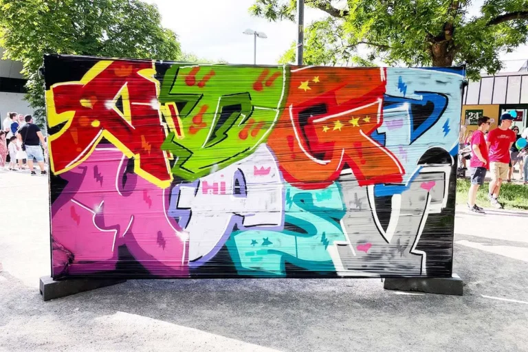 Fertige bunte Graffiti-Buchstaben auf einem Bauzaun beim Bürgerfest West in Stuttgart, im Hintergrund Kletterwand und Besucher