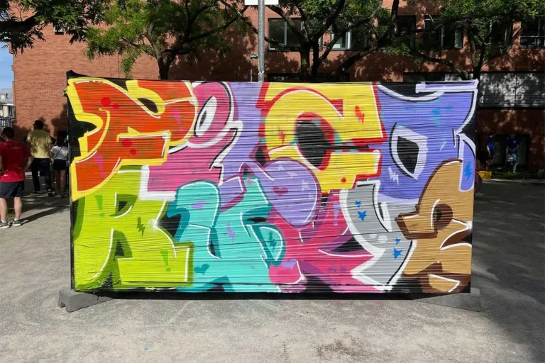 Fertige bunte Graffiti-Buchstaben auf einem Bauzaun beim Bürgerfest West in Stuttgart, im Hintergrund Kletterwand und Besucher