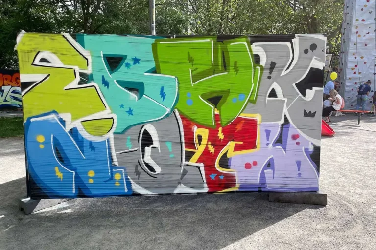 Fertige bunte Graffiti-Buchstaben auf einem Bauzaun beim Bürgerfest West in Stuttgart, im Hintergrund Kletterwand und Besucher