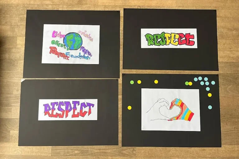 Gemalte Schülerentwürfe auf schwarzem Tonpapier mit Respekt-Schriftzügen, Peace-Zeichen und Friedenstauben
