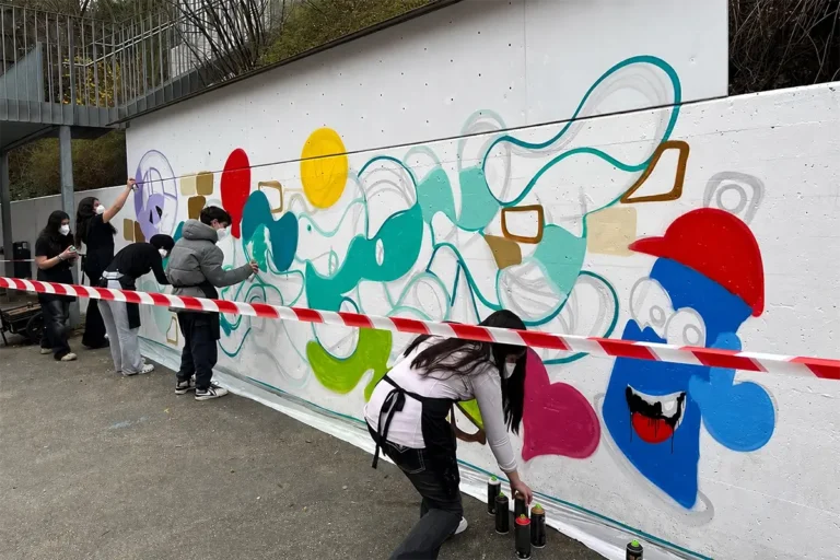 Schülerinnen und Schüler mit Masken sprühen bunte Formen an eine weiße Wand beim Schulprojekt in Leonberg