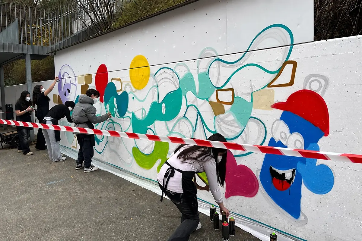 Schülerinnen und Schüler mit Masken sprühen bunte Formen an eine weiße Wand beim Schulprojekt in Leonberg