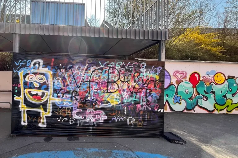 Fertiges Graffiti mit buntem Respekt-Schriftzug, Peace-Zeichen und Sprühdosen-Figur auf der Pausenhofwand der Pestalozzischule Leonberg